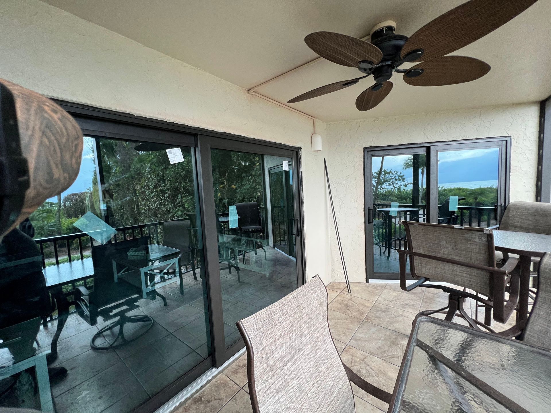 Patio with sliding glass doors, outdoor furniture, ceiling fan, and view of trees.