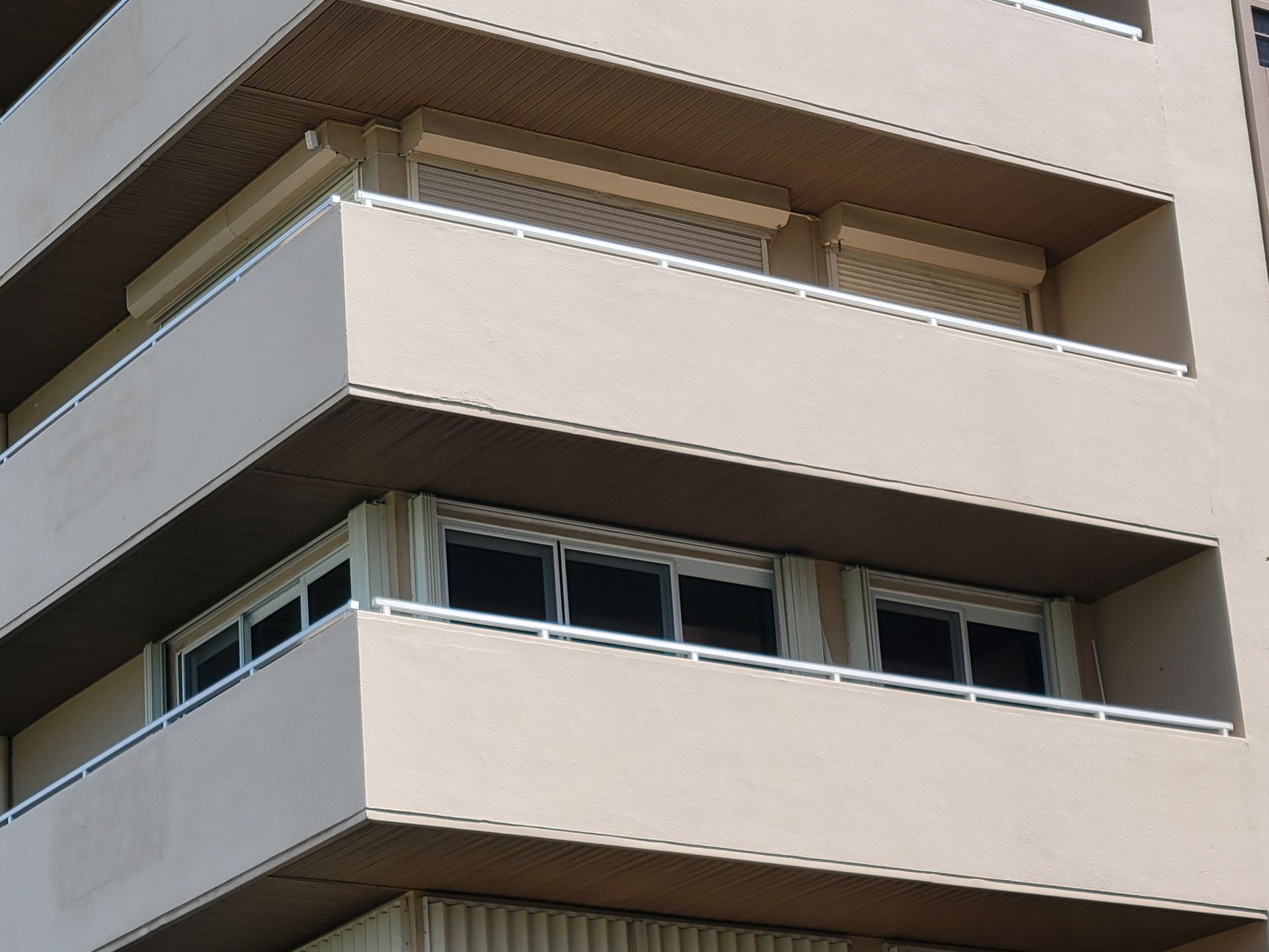 Tan building with balconies; windows visible behind railings.