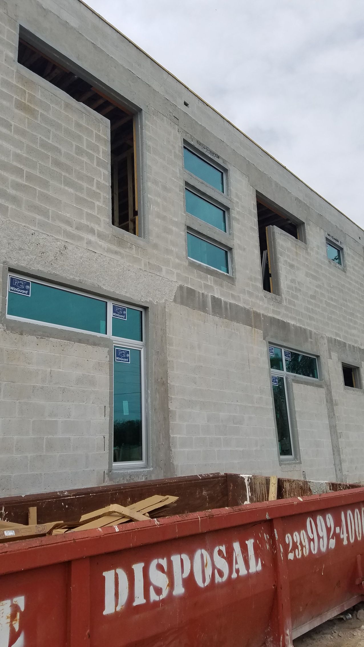 Exterior of a two-story cinder block building under construction, with windows and a red disposal bin.
