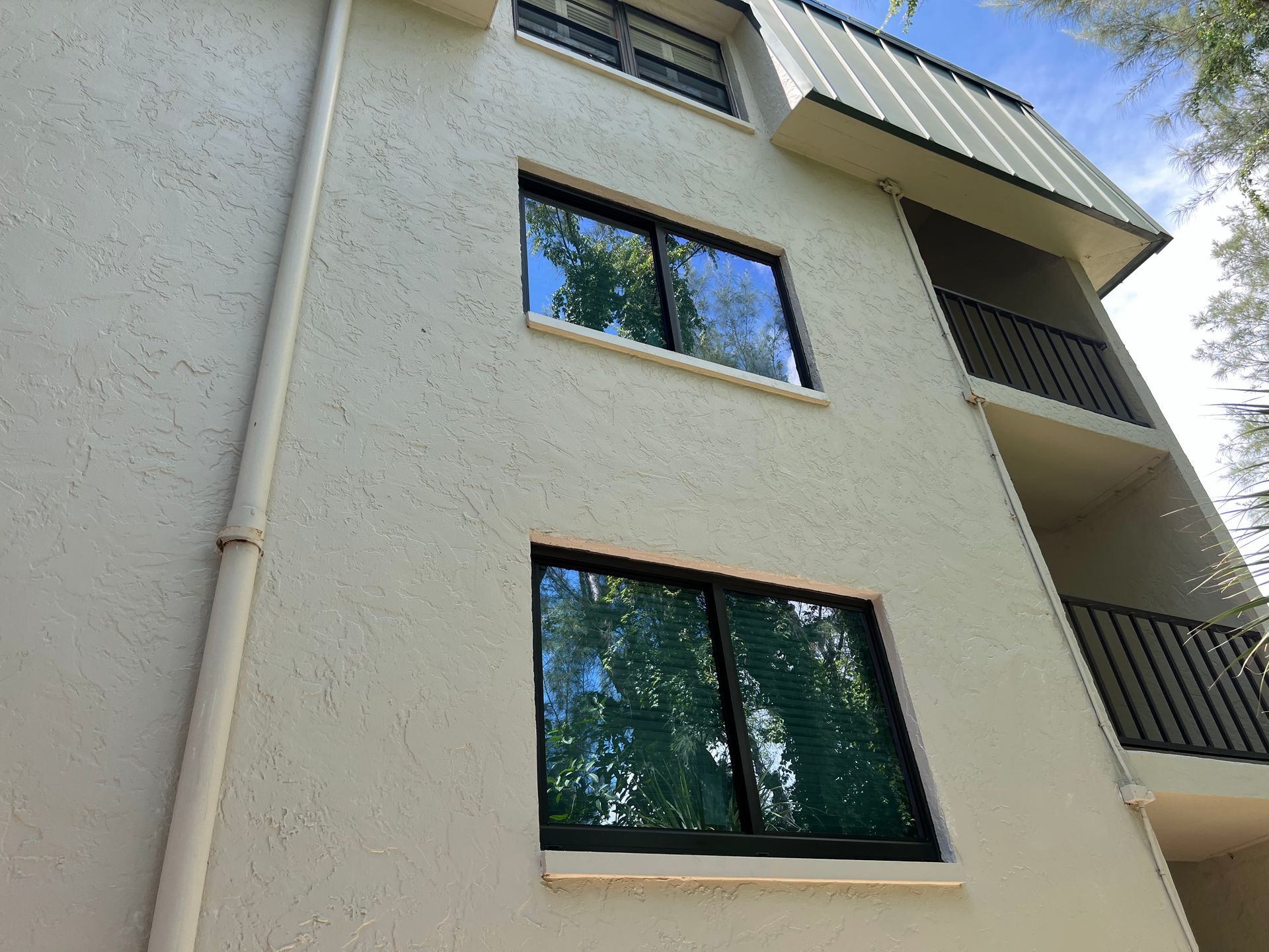 Beige stucco building with black-framed windows and a metal roof; balconies on the right.