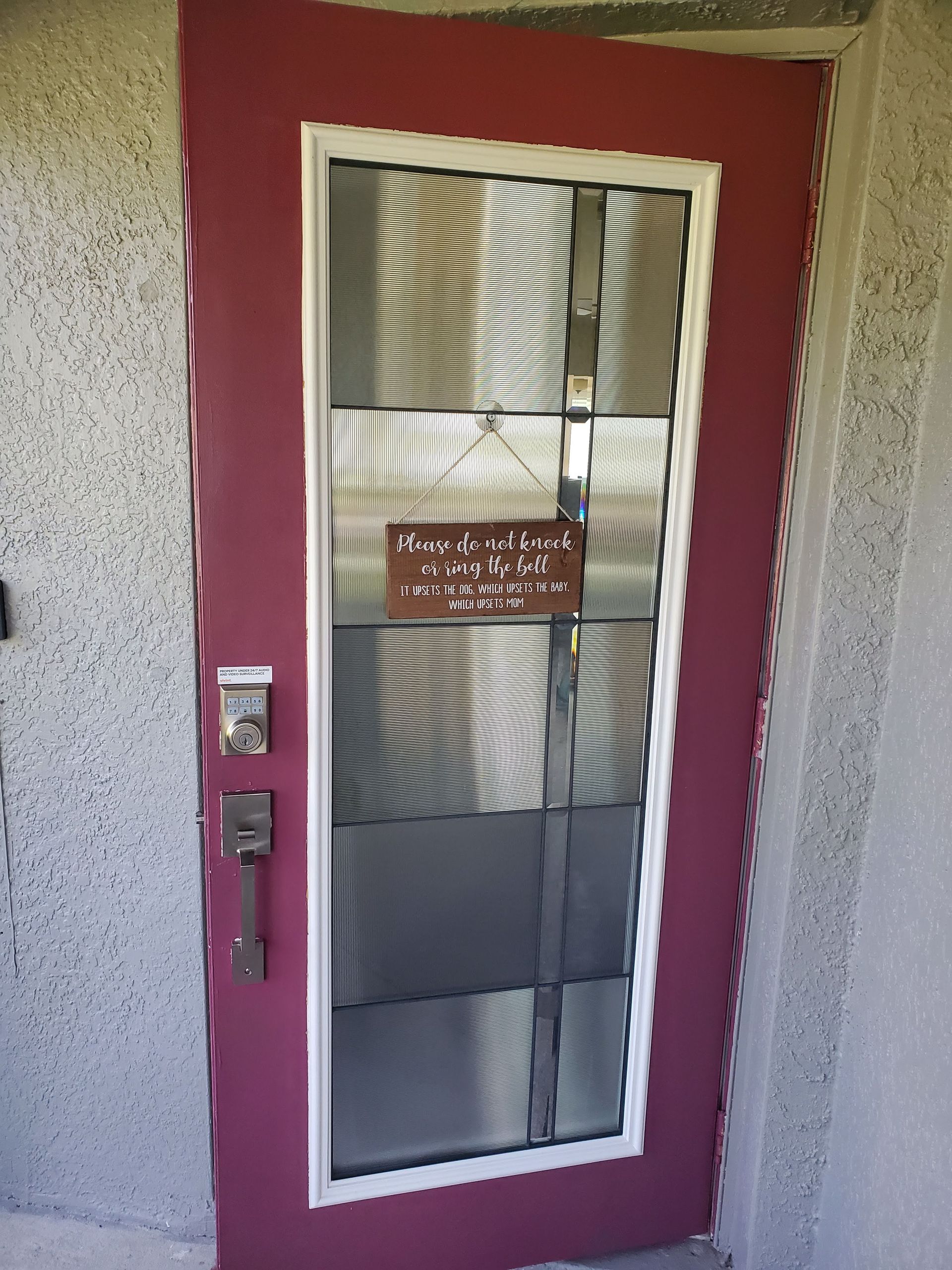 Red door with a white-framed screen, sign and handle on a stucco wall.