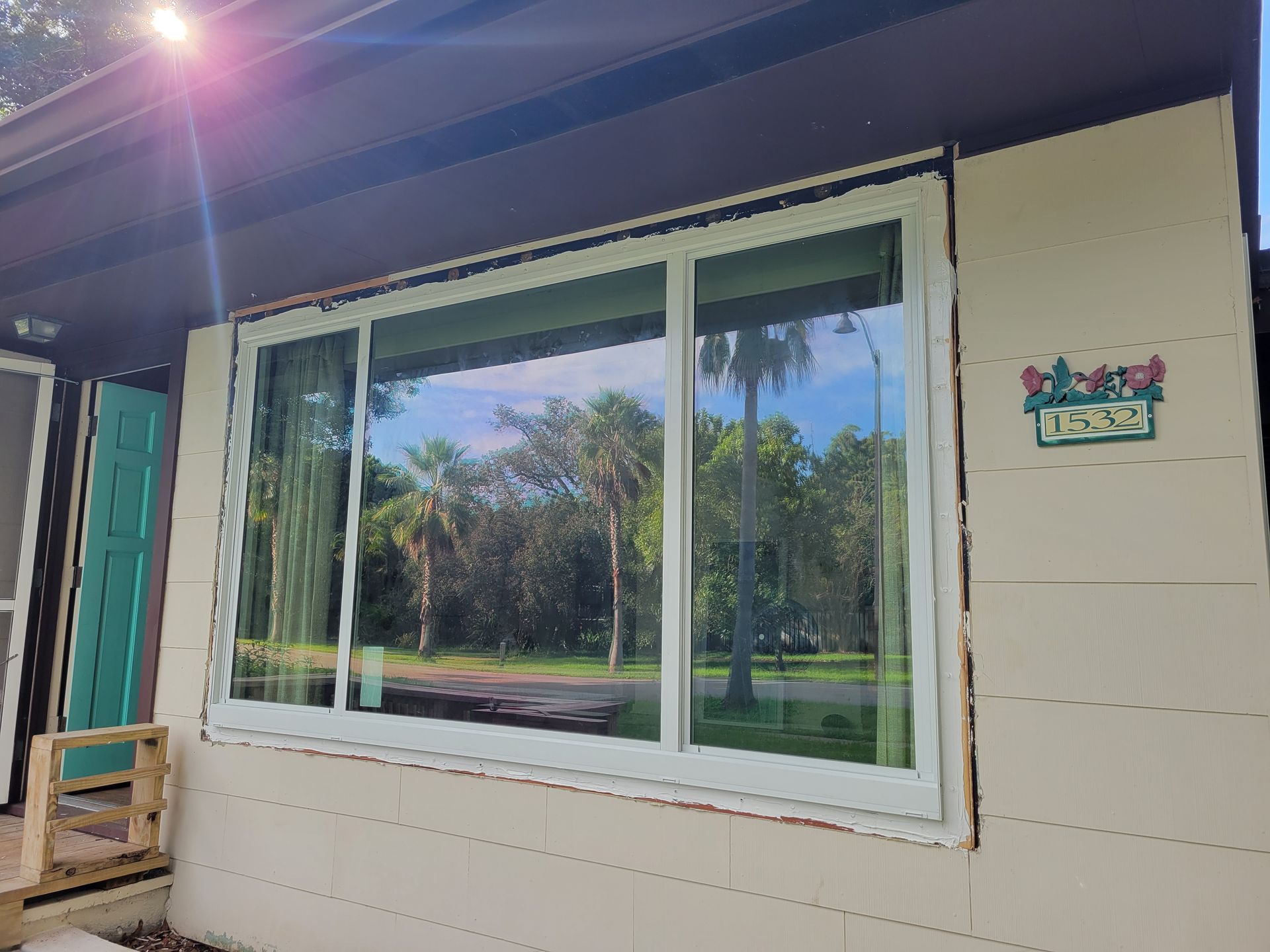 A house exterior with a large window reflecting palm trees and a bright sun.