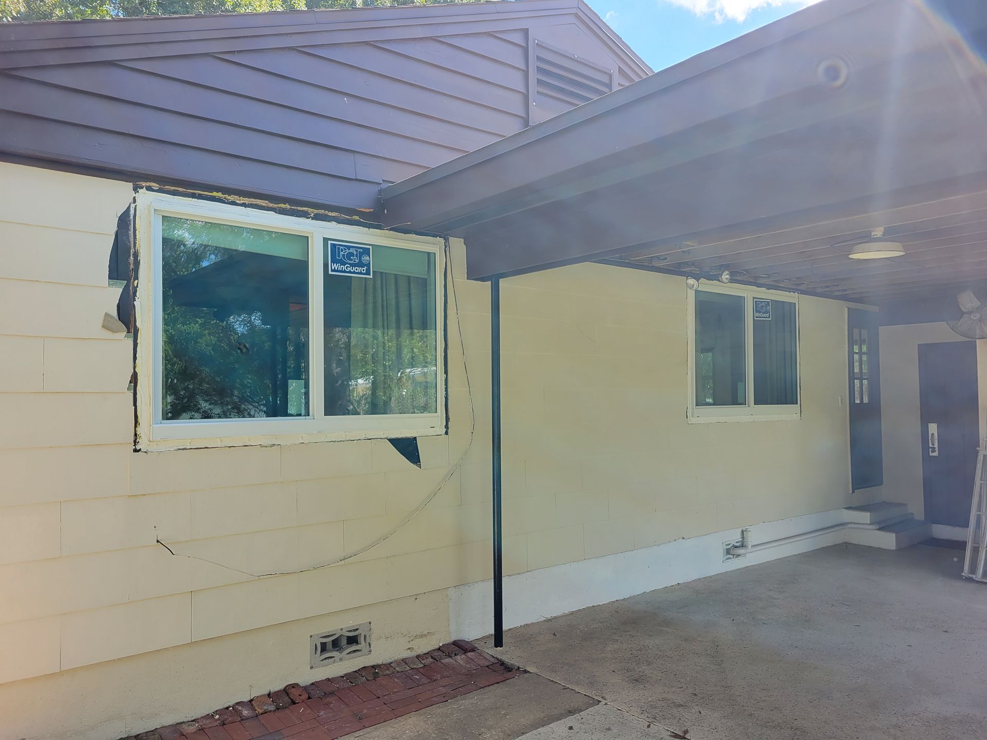 Exterior of a beige house with a brown roof and carport, new windows installed.
