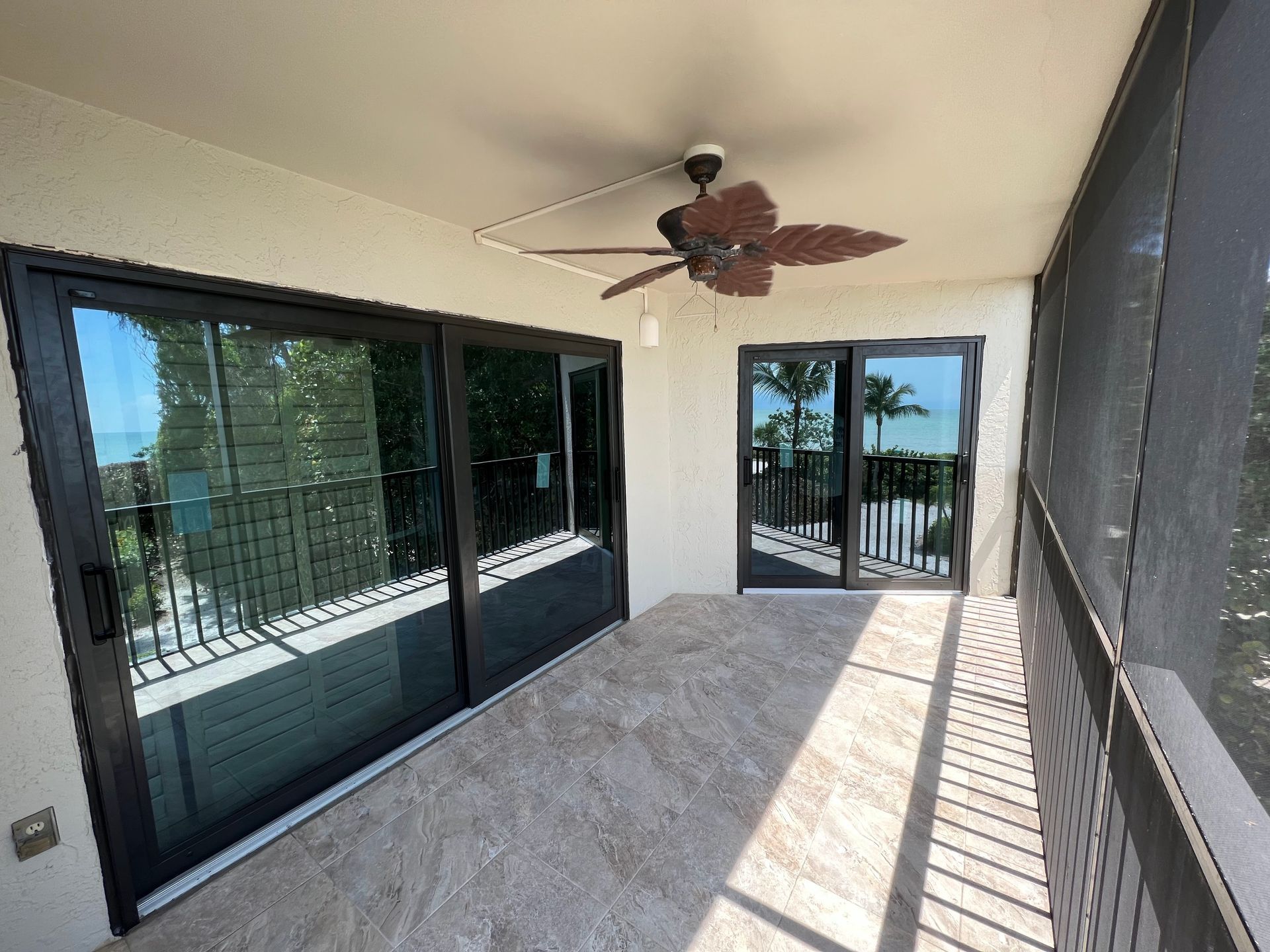 Balcony with black sliding doors, tile floor, and ceiling fan; overlooking a view of water and trees.