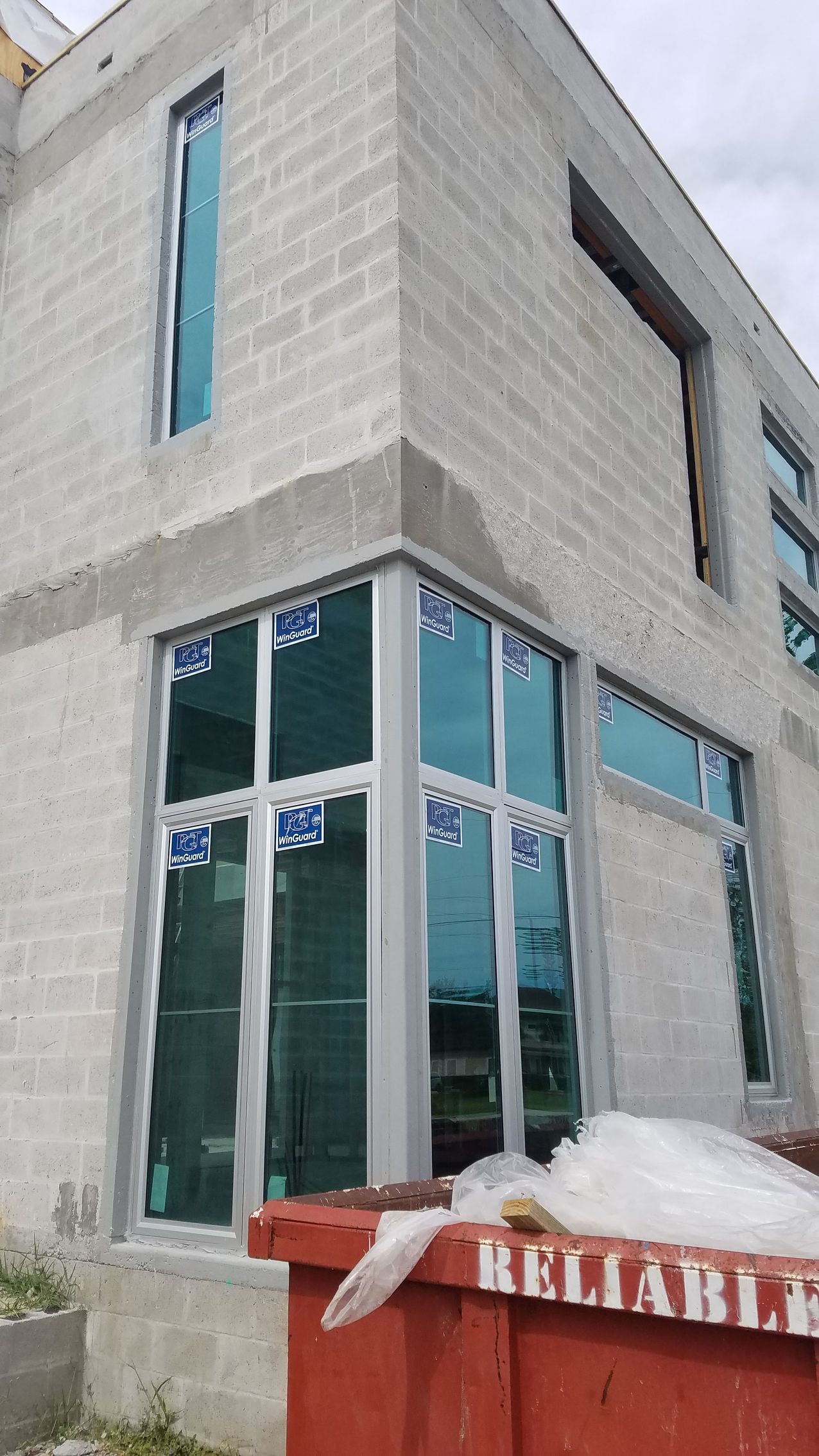 Building exterior under construction with concrete block walls, windows, and a red dumpster.
