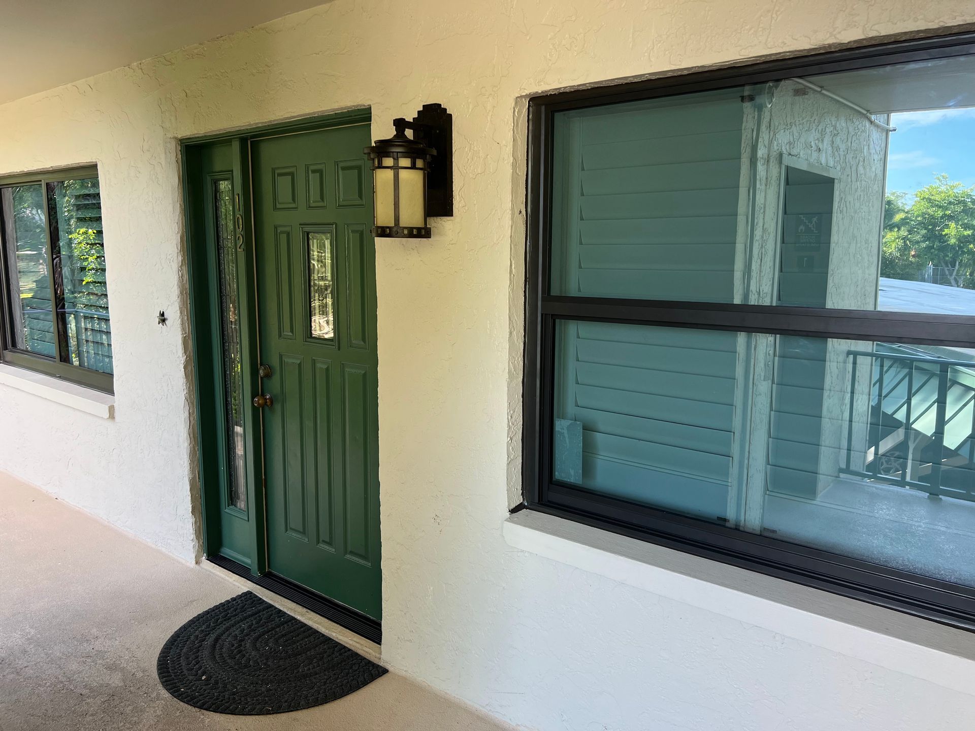 Green front door with sidelight, flanked by black-framed windows on white stucco building.