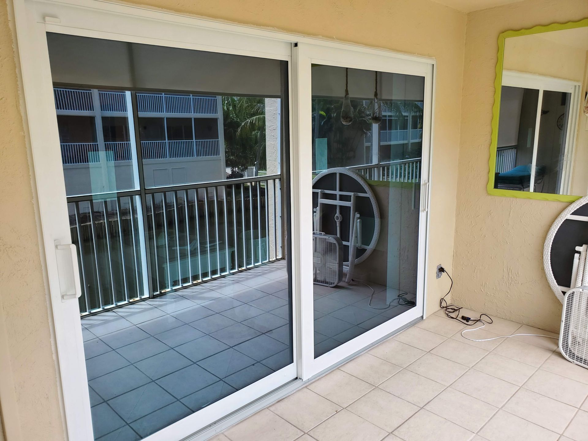 White framed sliding glass doors open to a balcony with a railing, reflecting surroundings.
