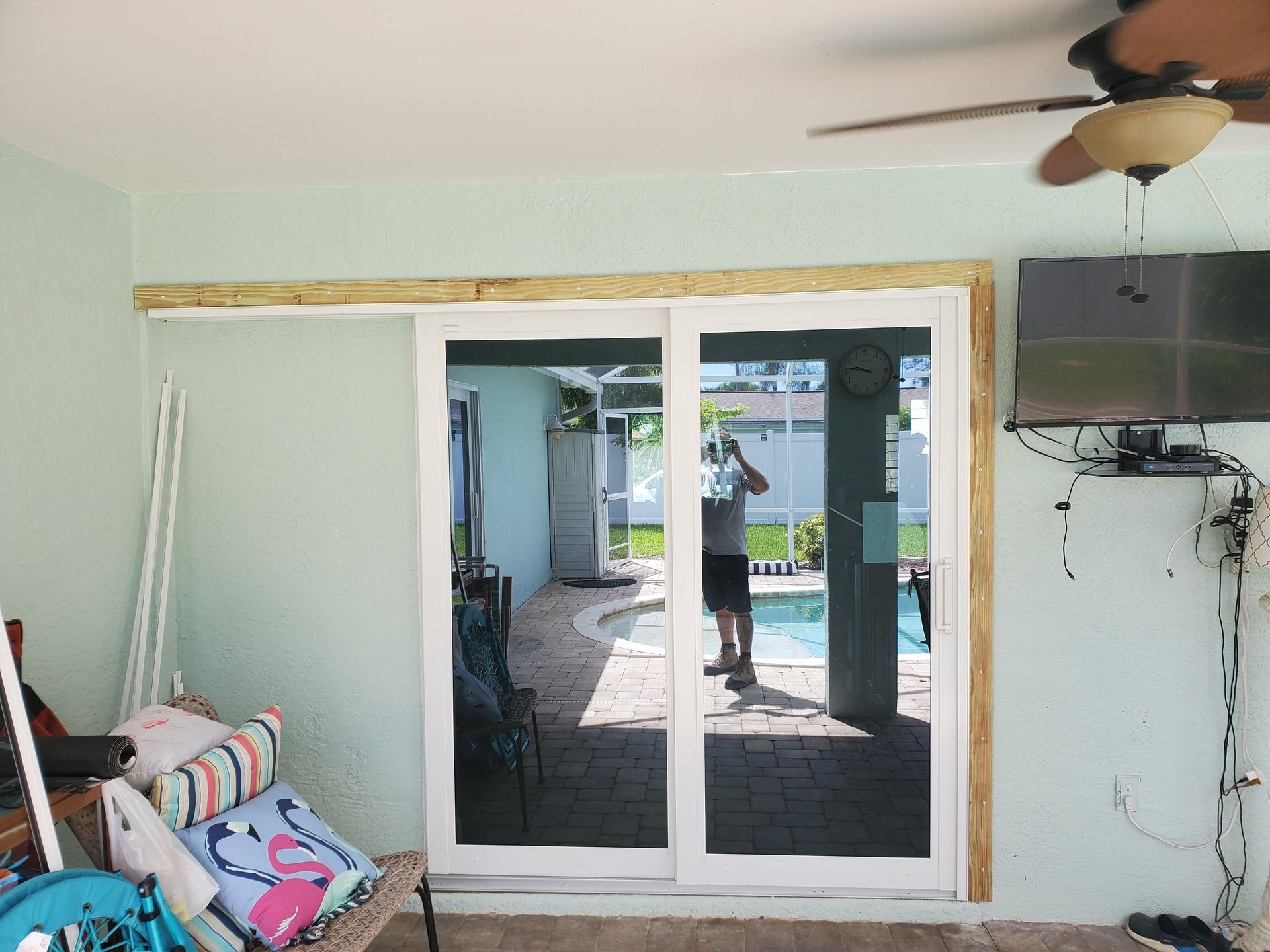 Sliding glass doors open to a pool area. A person is reflected in the glass. White doors, light blue walls, and a light brown frame.