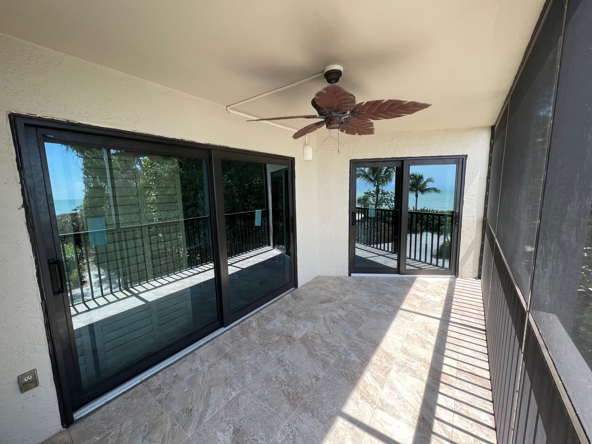 Patio with sliding doors, ceiling fan, and tiled floor; black frames, beige walls, view of water.