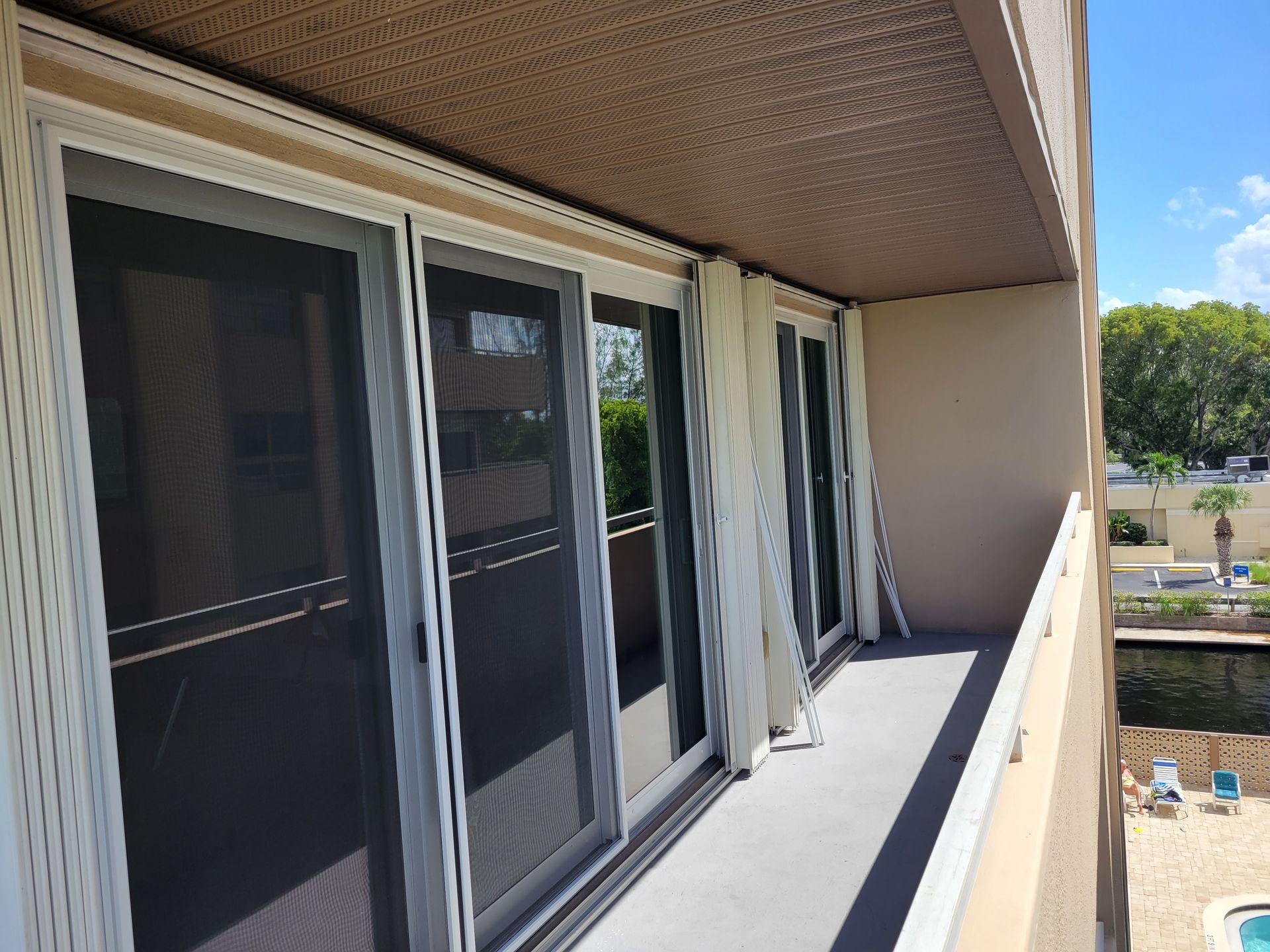 Balcony with sliding glass doors, white curtains, and a view of a pool on a sunny day.