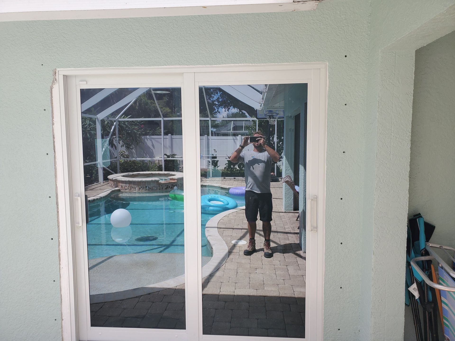 Man reflected in sliding glass door, standing by a pool.