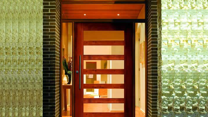 Wooden front door with glass panels framed by brick and textured walls.