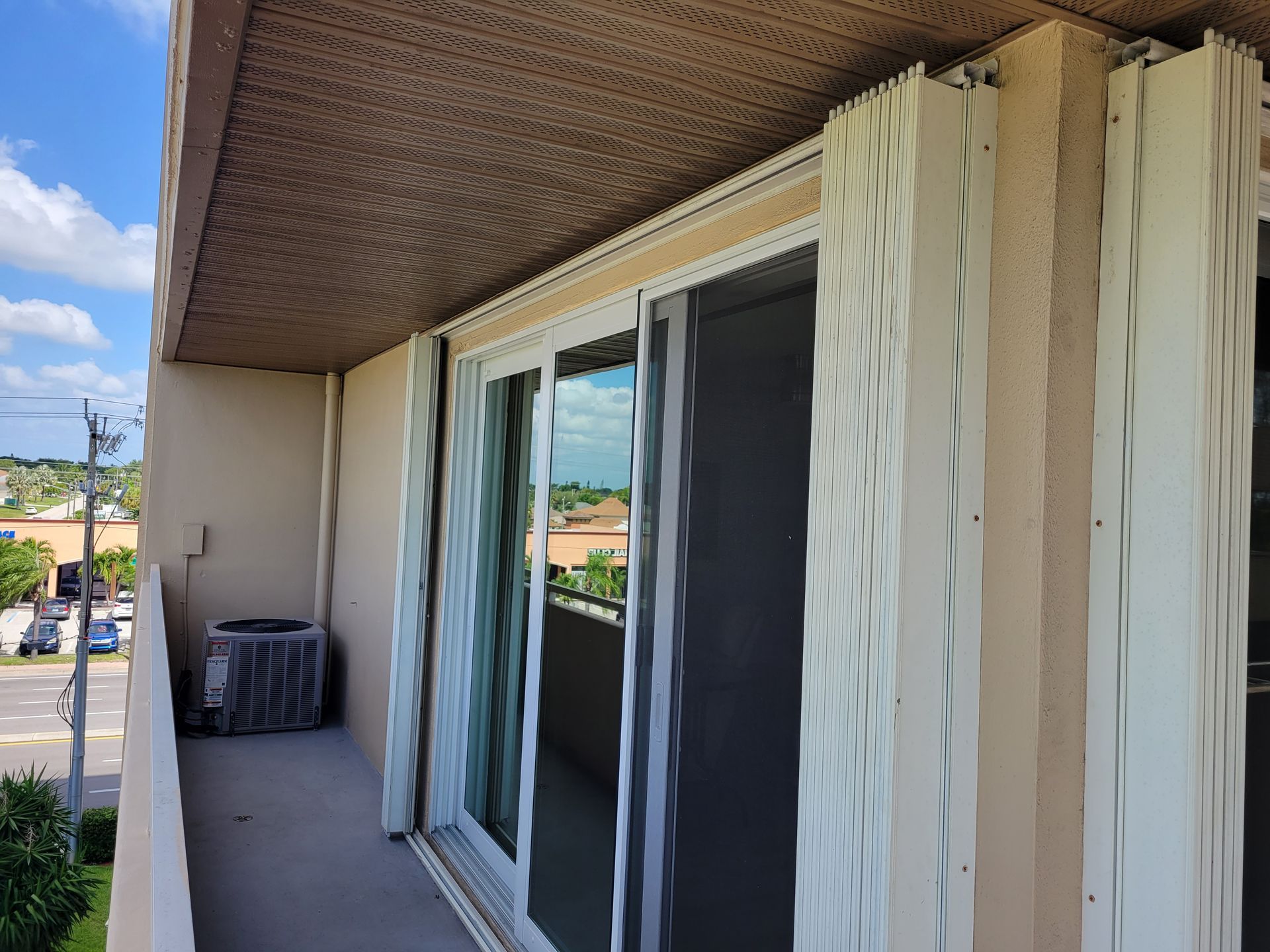 Balcony with sliding glass doors and accordion hurricane shutters; building exterior.
