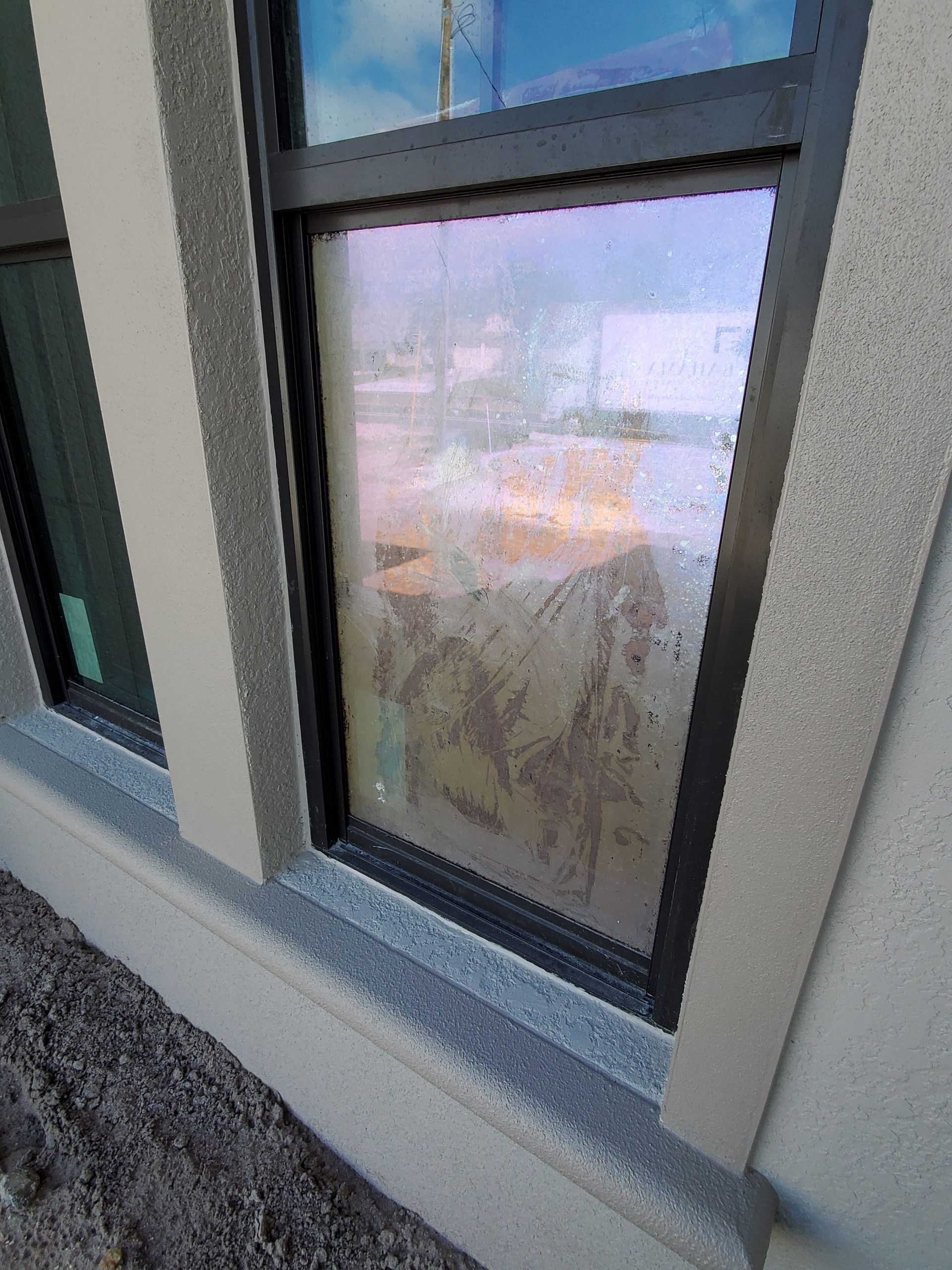 Window with condensation; black frame, light-colored building exterior.