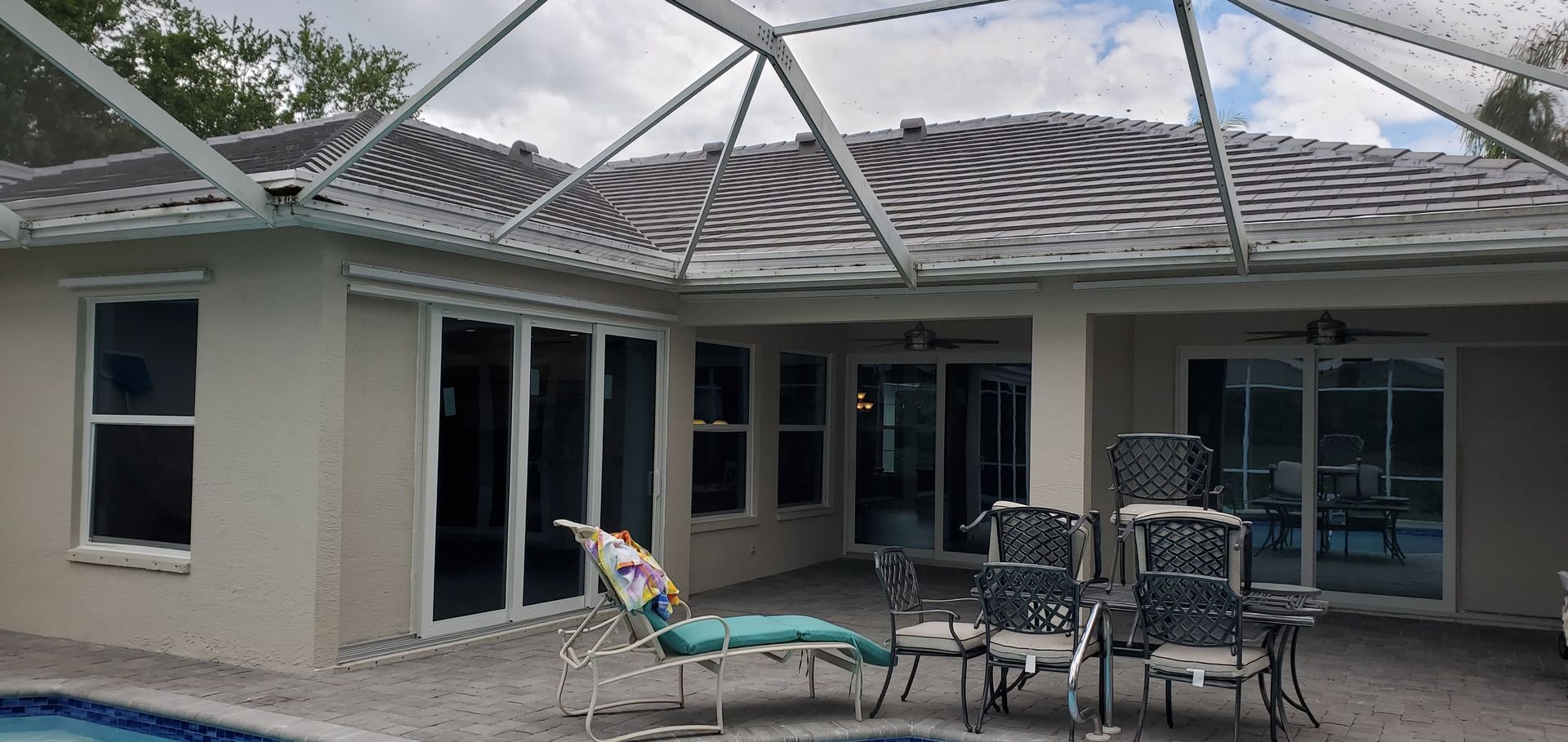 Back patio with chairs and a pool view. A glass roof covers the area.