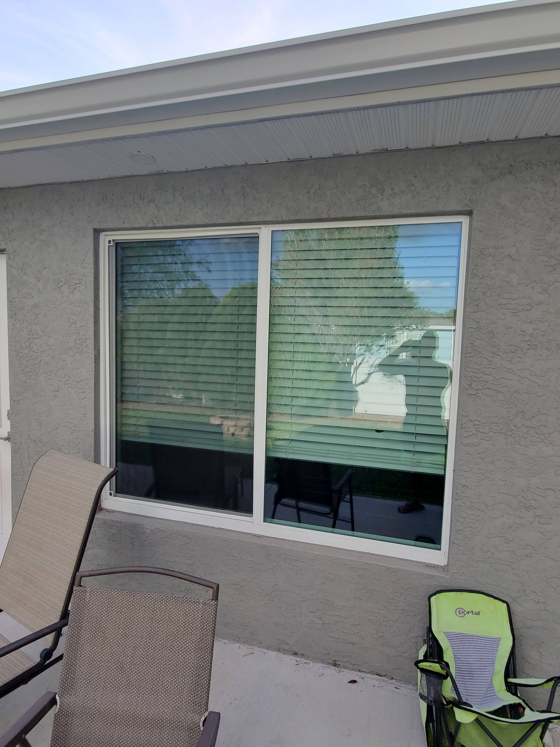 Window with blinds on a stucco exterior with patio furniture.