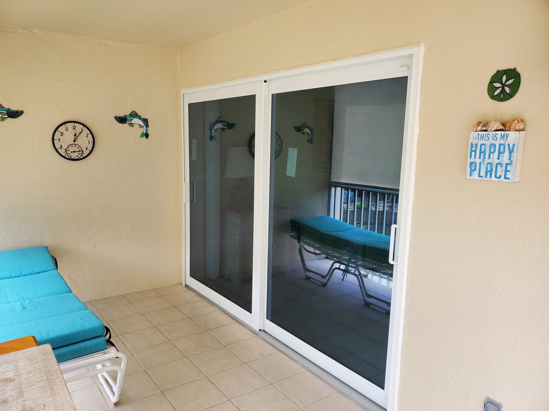 Sliding glass doors open to a patio with a chaise lounge and beach-themed decor on the wall.