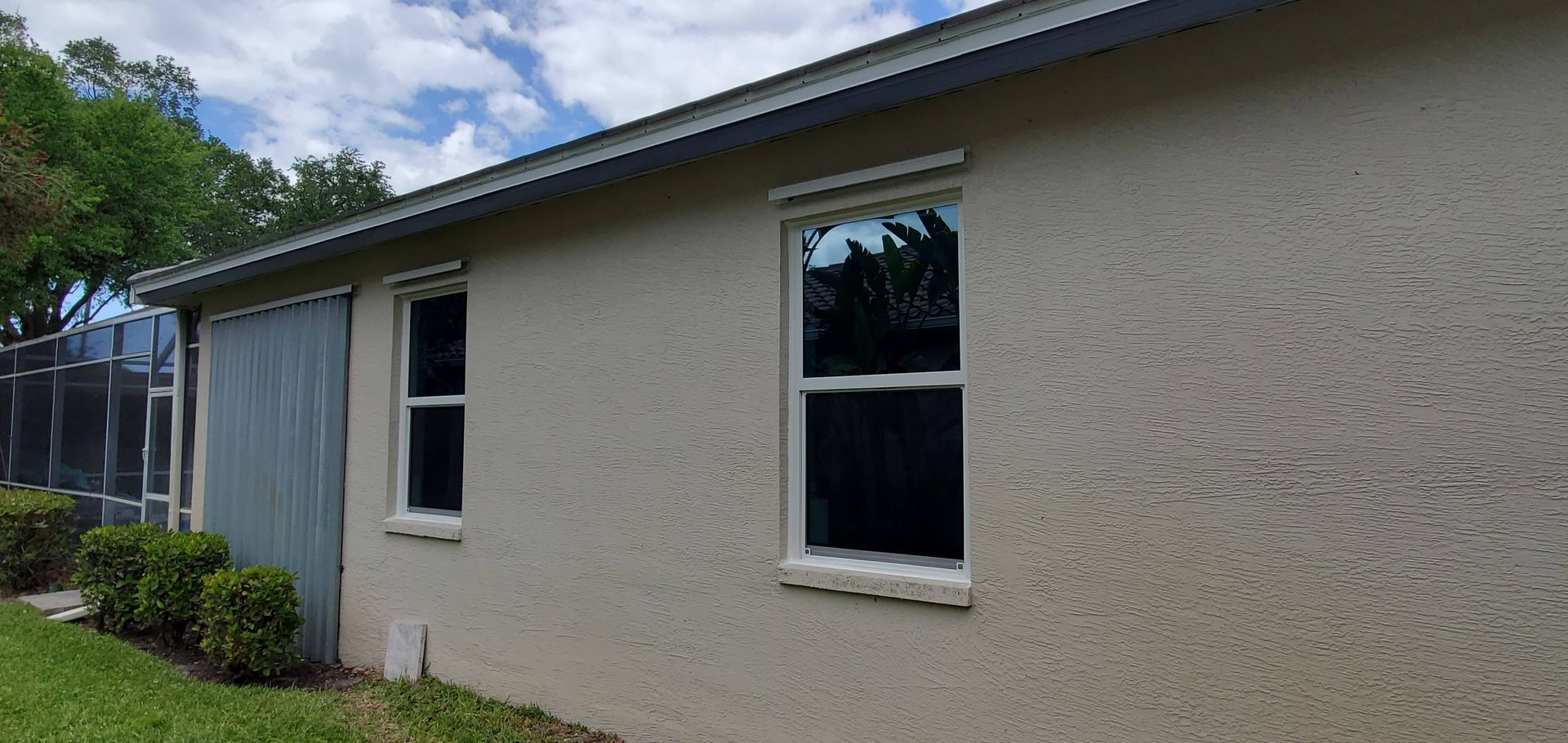 Exterior view of a stucco house with two windows. Green lawn and blue sky in the background.