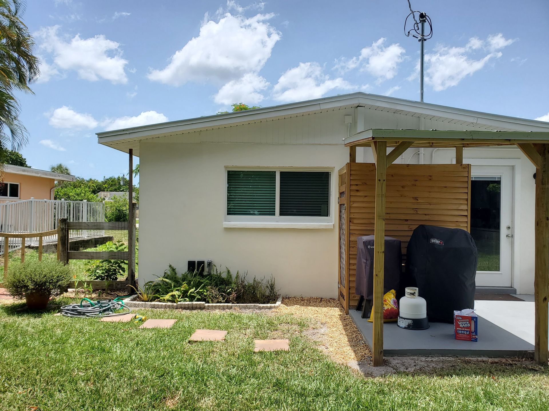 Small backyard with a white house, a wooden pergola, and a grill.