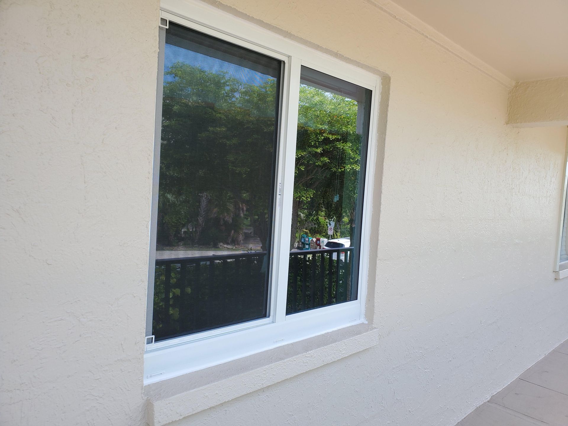 White-framed window on a stucco wall. Reflects trees and a balcony.
