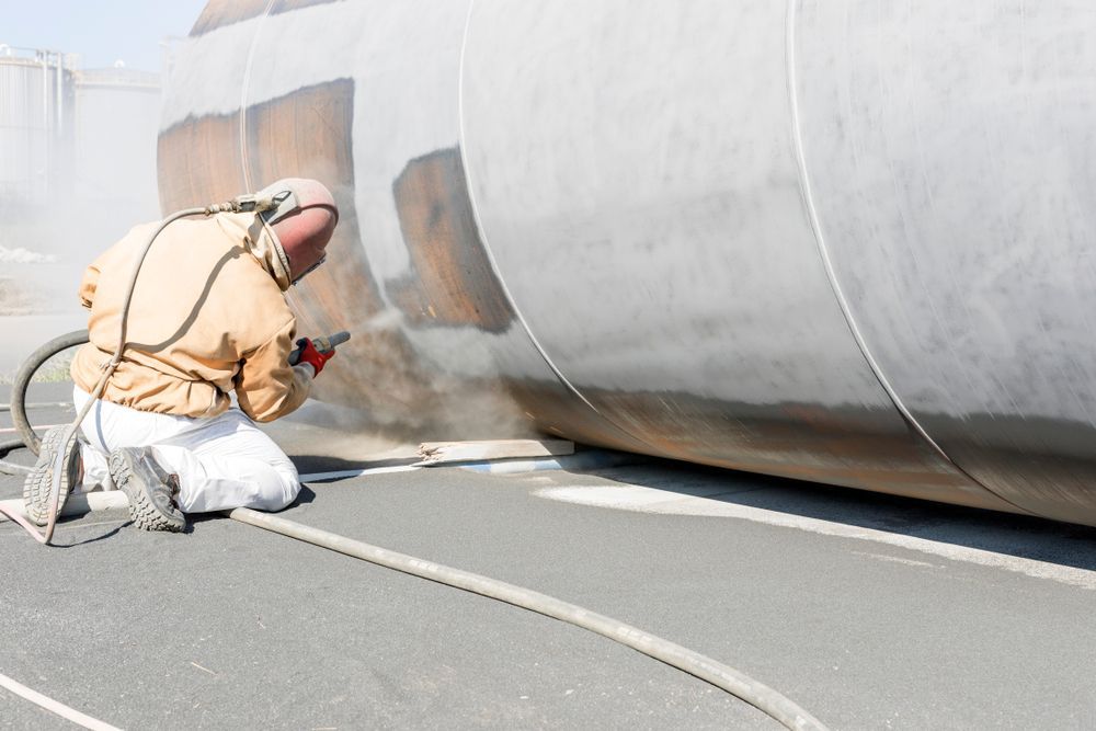A Man Is Sandblasting A Large Metal Object — Rockhampton Powdercoating & Fence Panels in Park Avenue, QLD