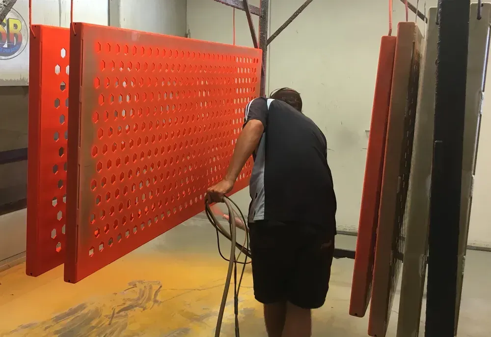A Man Is Standing In Front Of A Red Wall — Rockhampton Powdercoating & Fence Panels in Park Avenue, QLD
