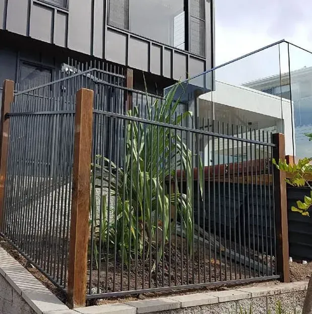 A Metal Fence With Wooden Posts Is In Front Of A Building — Rockhampton Powdercoating & Fence Panels in Park Avenue, QLD