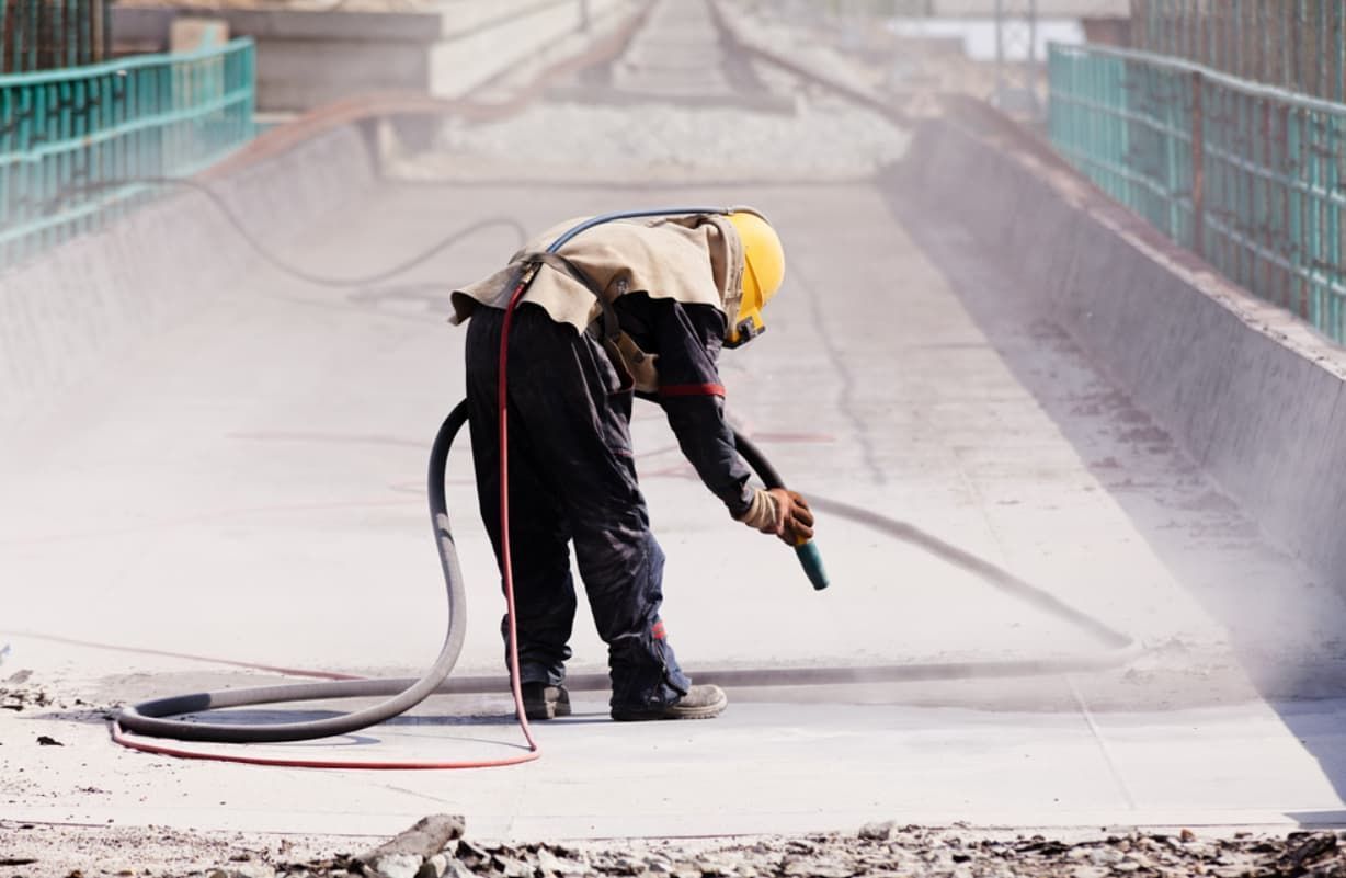 A Man Is Sandblasting A Concrete Surface With A Machine — Rockhampton Powdercoating & Fence Panels in Park Avenue, QLD