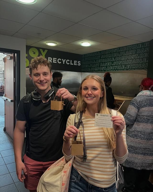 A man and a woman are posing for a picture in front of a sign that says box recycles.