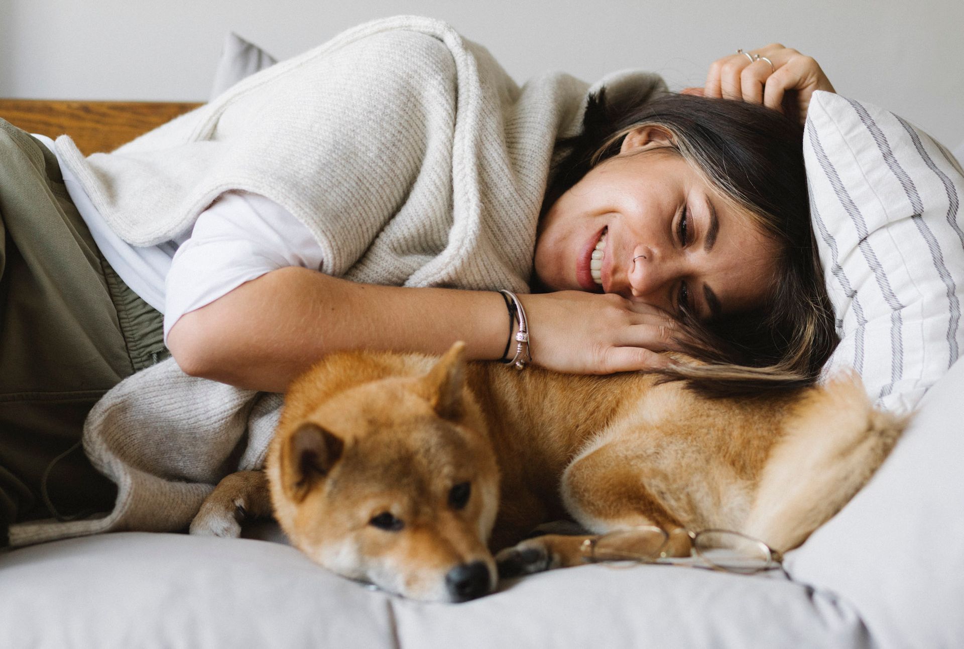A person resting on a couch, gently cuddling a tan Shiba Inu dog.