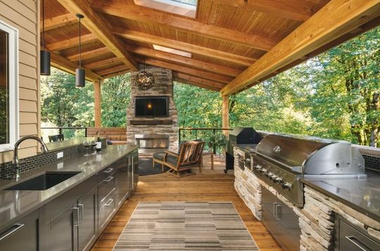 A large outdoor kitchen with stainless steel cabinets , a sink , a grill and a fireplace.