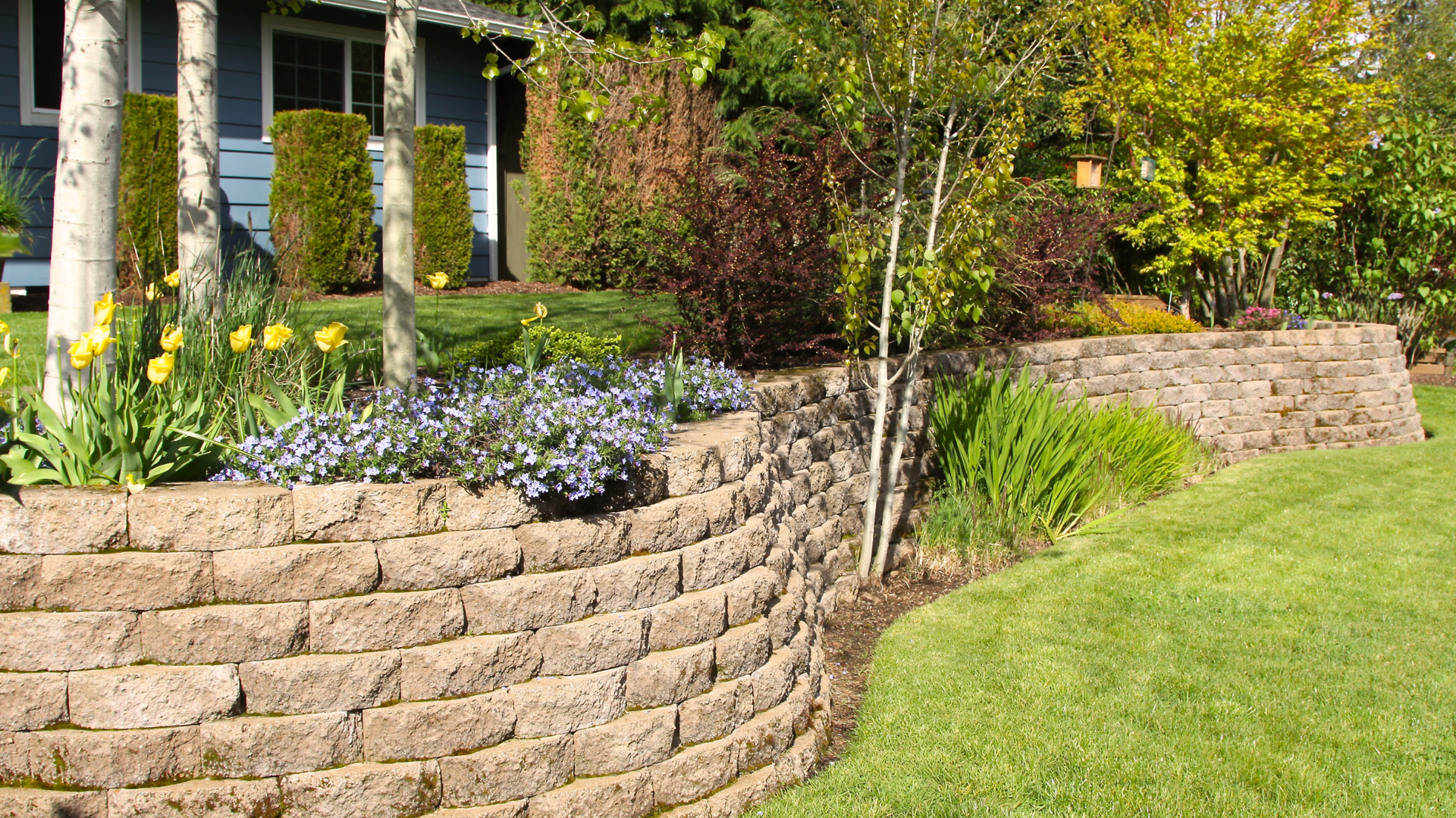 A stone wall surrounds a lush green lawn in front of a house.