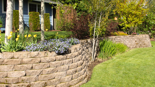A stone wall surrounds a lush green lawn in front of a house.