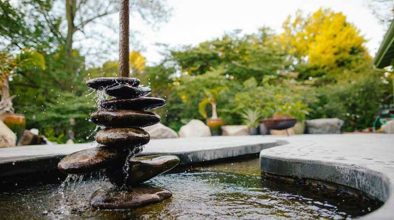 A fountain in a garden with a stack of rocks in the middle of it.