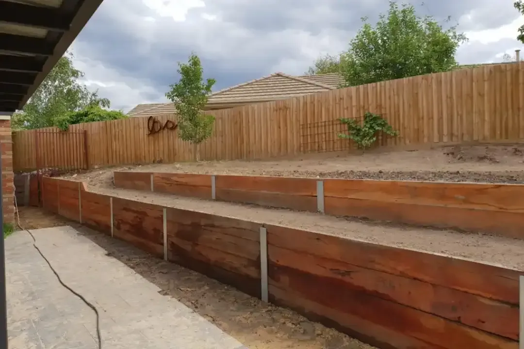 A wooden retaining wall with a wooden fence in the background.