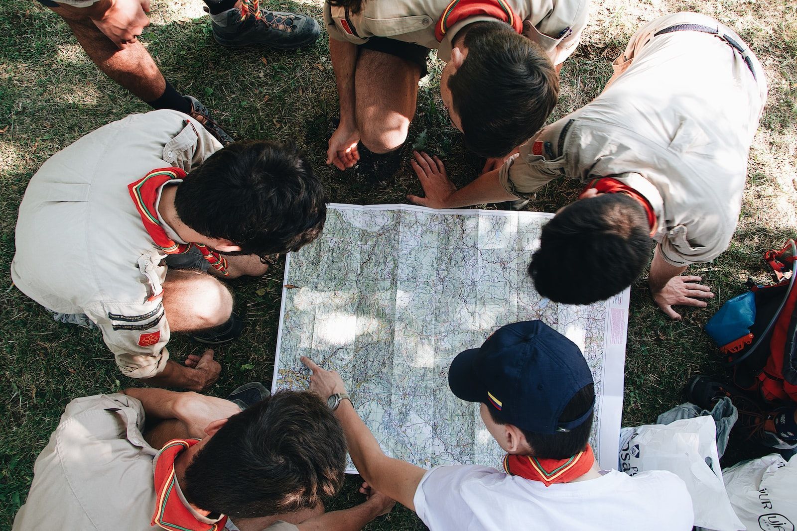 Group of people in scout uniforms examining a map on a grassy surface.