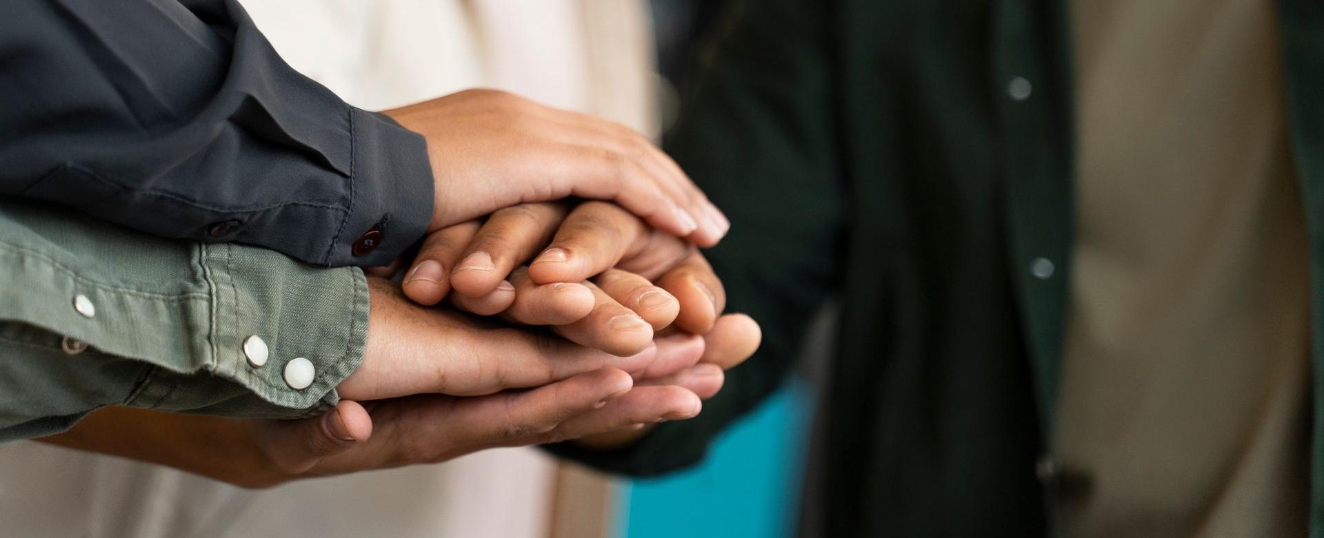 Hands stacked together, showing unity and support. The clothing colors are green, black, and beige.