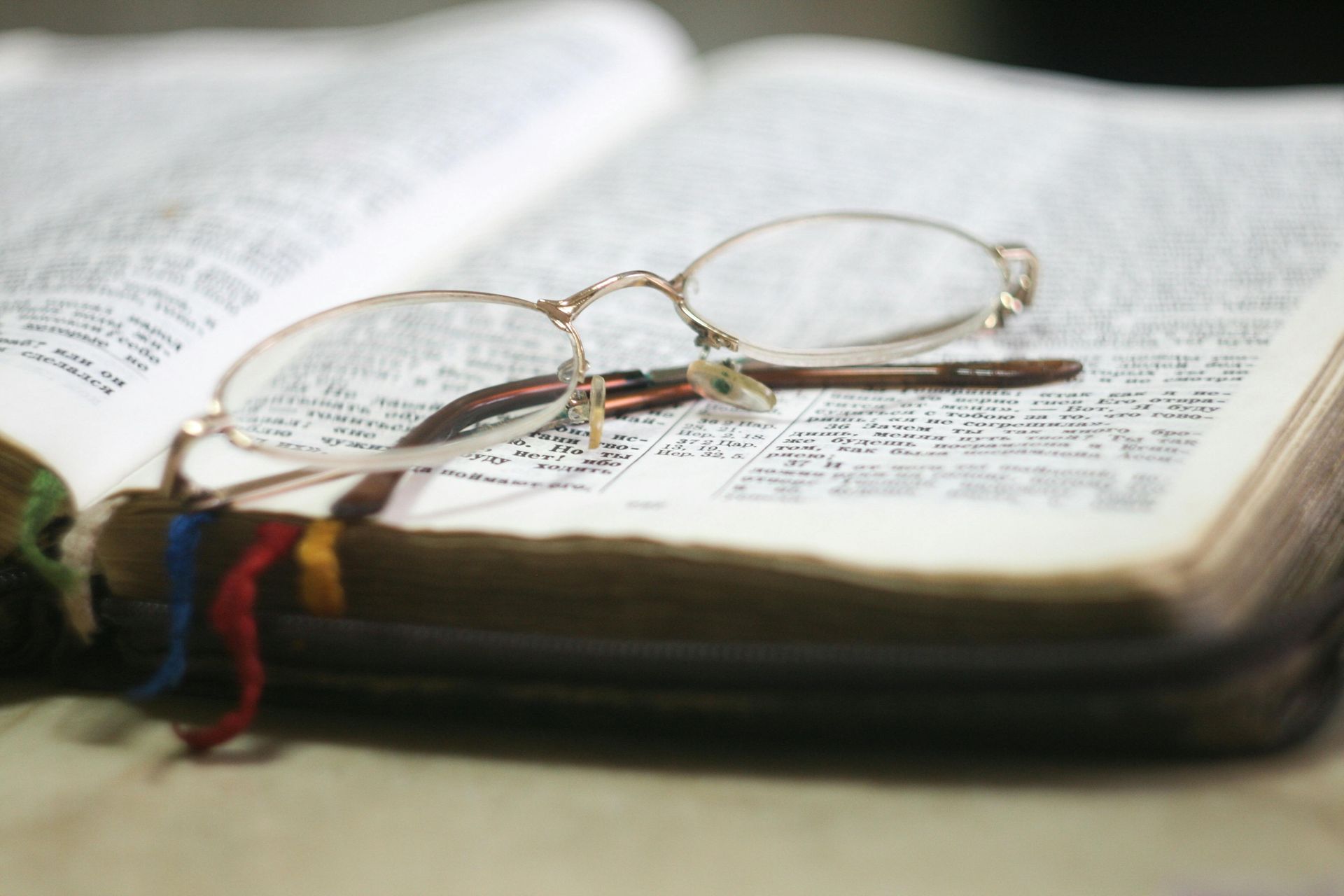 Open book with reading glasses resting on it, several colored ribbons marking pages.