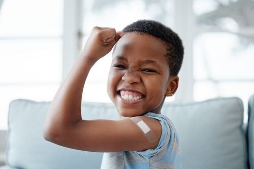Smiling child flexes arm with bandage, celebrating vaccine.