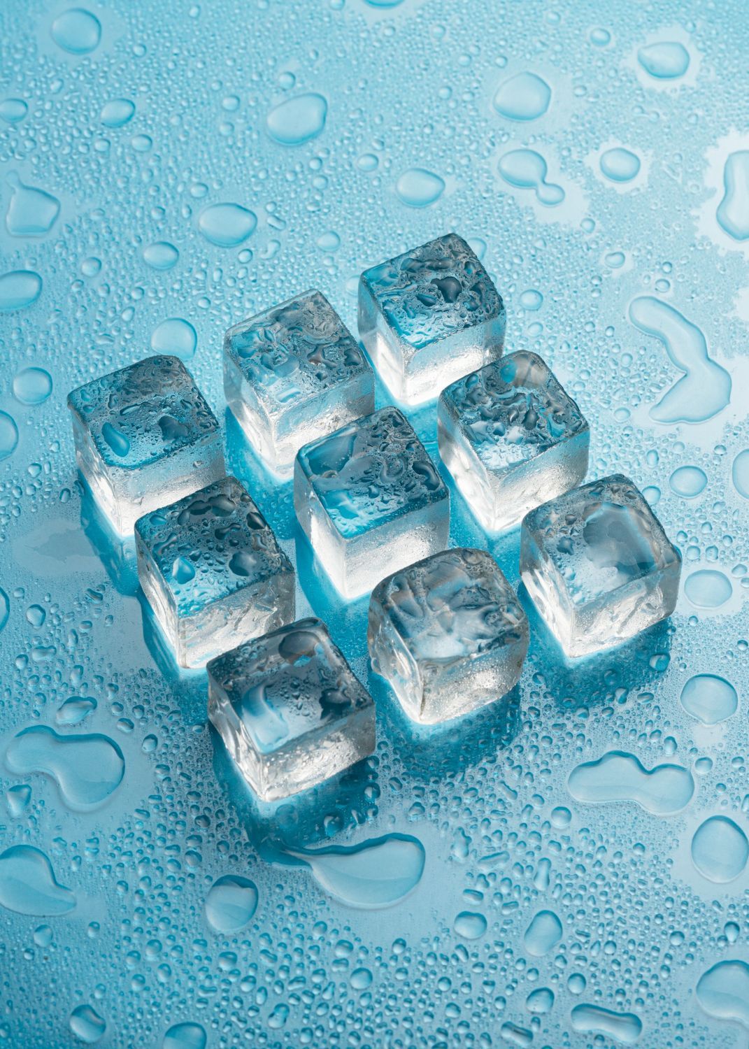A group of ice cubes sitting on top of a blue surface with water drops.