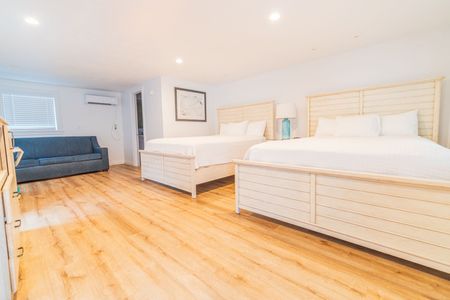 Bright white hotel room with two queen beds, sofa, and light wood flooring.