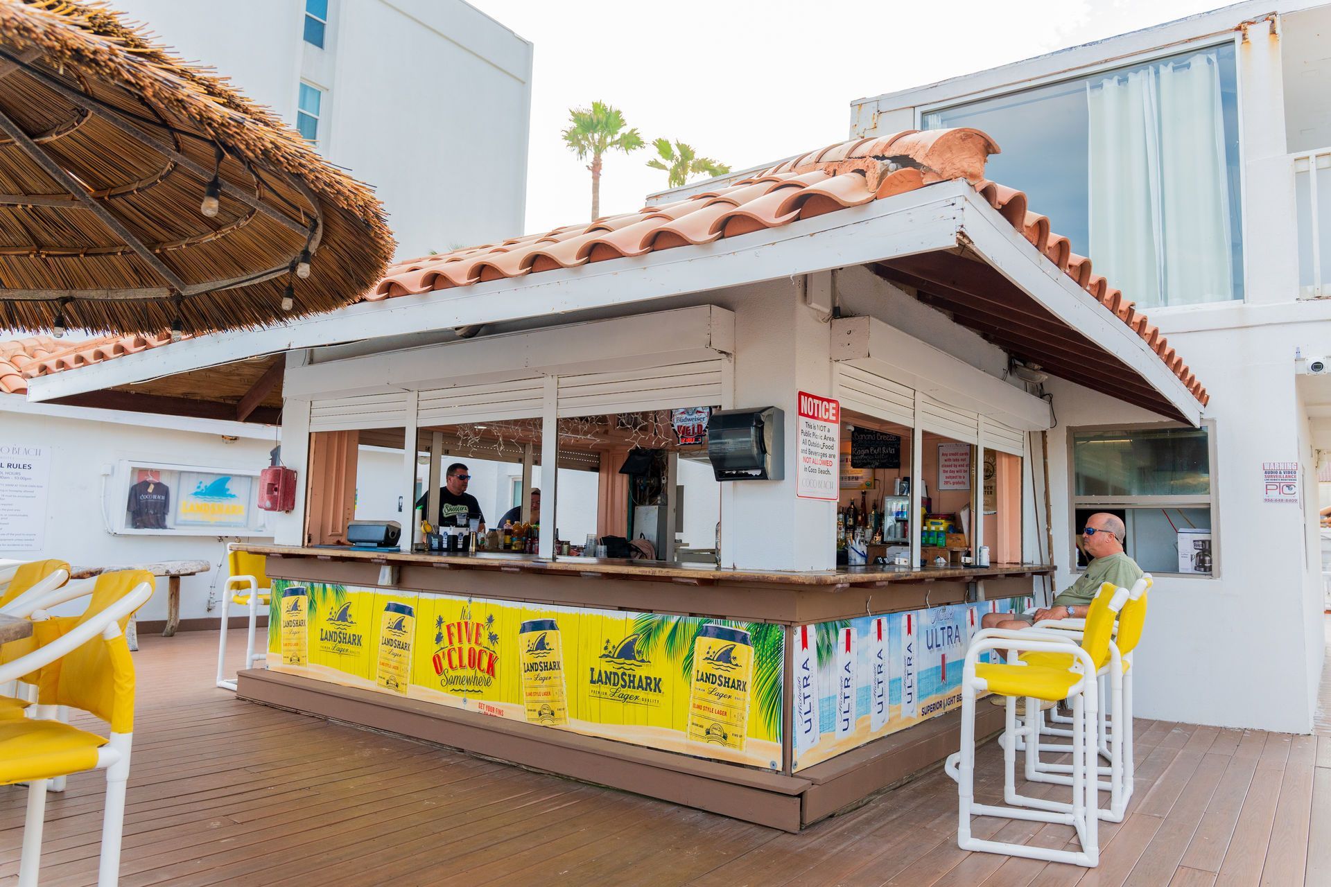 Beachside bar with tiled roof, drinks being served, patrons seated at the bar.