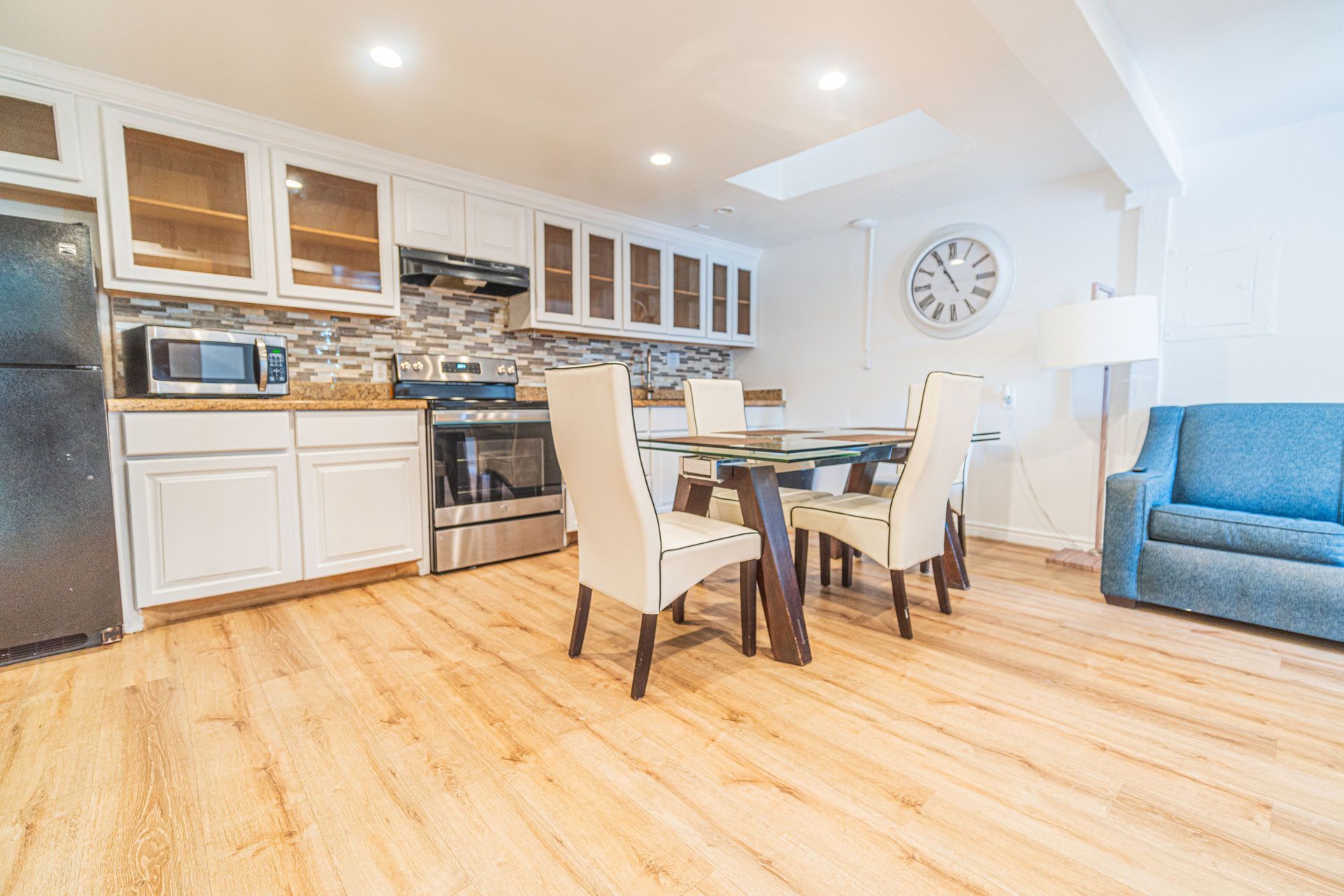 Kitchen with white cabinets, stainless steel appliances, dining table, and blue sofa.