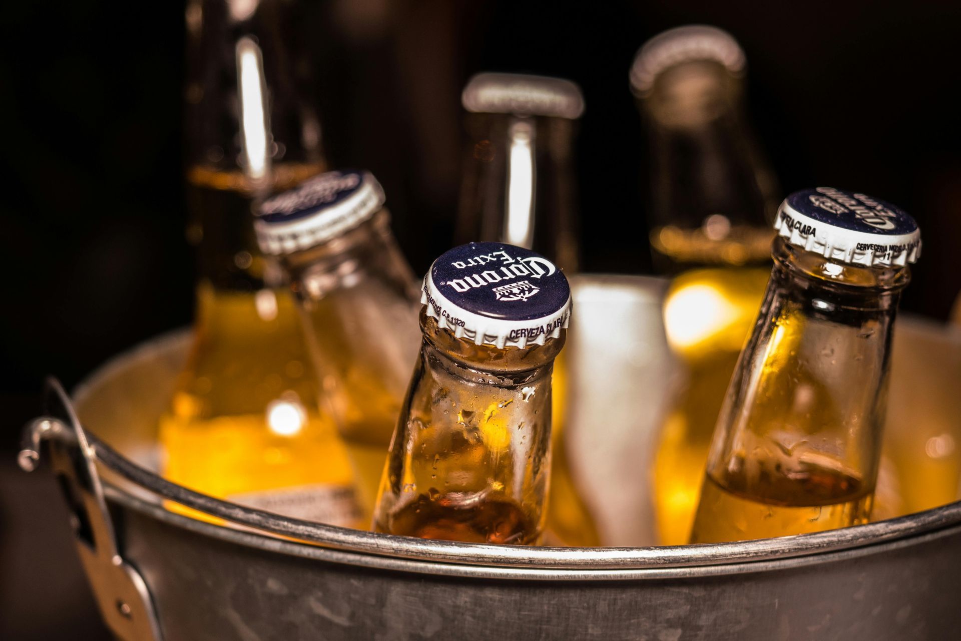 Bottles of beer in a metal ice bucket. Brown glass, silver caps, and yellow liquid.