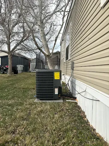 Air conditioner unit next to a house with beige siding, grass, and a tree.