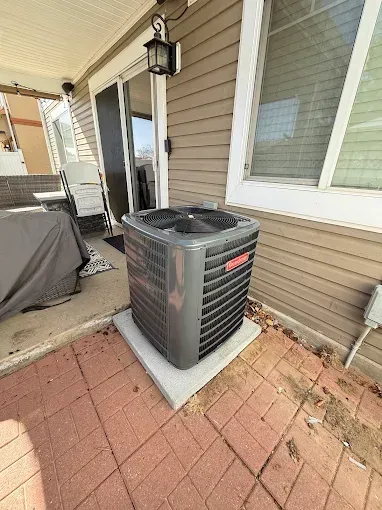 Outdoor Goodman air conditioning unit on a concrete pad next to a window and sliding door.