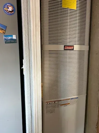 Coleman furnace in a narrow space next to a refrigerator.