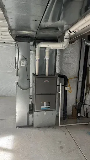 Furnace in basement with ductwork and PVC pipes, silver and white.
