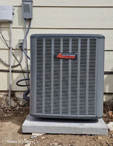 Gray Amana air conditioner unit on a concrete pad next to a beige house wall.