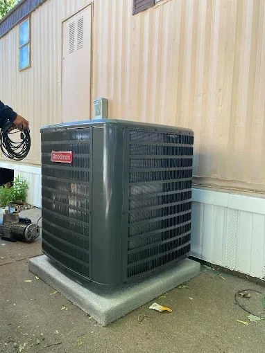 Dark gray Goodman AC unit on a concrete pad next to a light brown building.